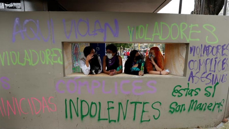 Varias mujeres conversan frente a una pared con grafitis pintados en las paredes de un Comando de Atención Inmediata (CAI) de la Policía durante unas protestas en Bogotá (Colombia).