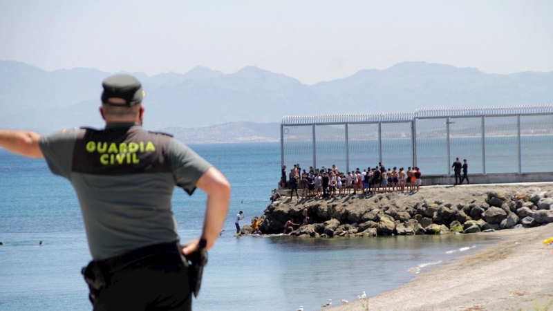 Un agente de la Guardia Civil observa a migrantes marroquíes llegados a nado este lunes a Ceuta.