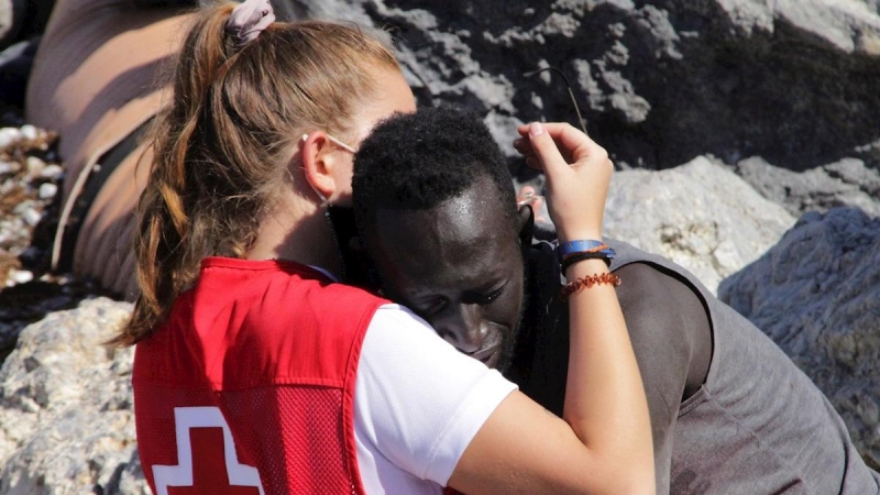 Una trabajadora de la Cruz Roja y un migrante que ha logrado cruzar uno de los espigones fronterizos de Ceuta.