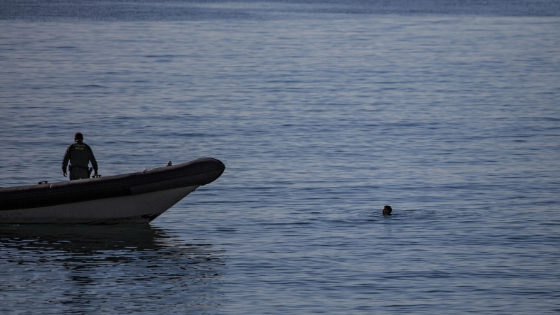 Una persona entra a nado a la playa de Tarajal en Ceuta, mientras que la Guardia Civil acude a socorrerlo.