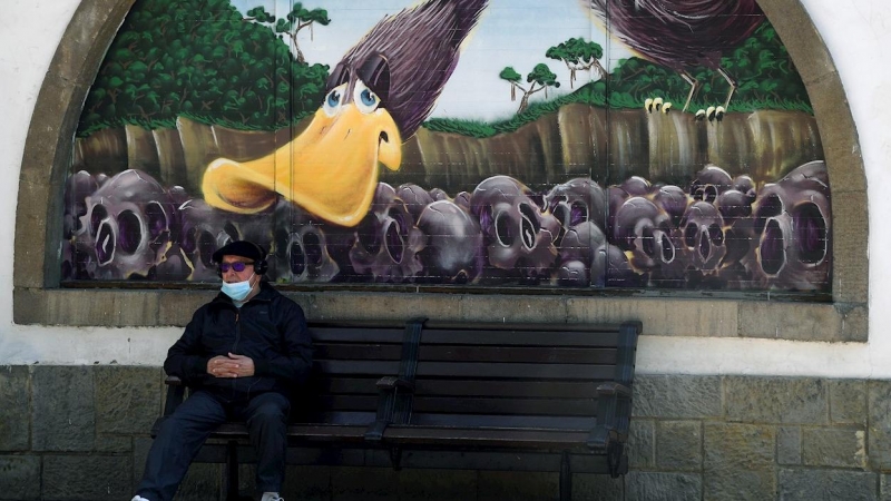 Un hombre con mascarilla sentado ante un grafiti de la Biblioteca Pública del Parque de San Francisco en el centro de Oviedo.