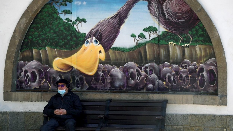 Un hombre con mascarilla sentado ante un grafiti de la Biblioteca Pública del Parque de San Francisco en el centro de Oviedo.