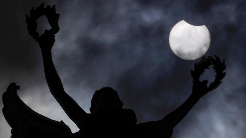 El eclipse solar parcial de este jueves se aprecia detrás de la estatua del parque del Jubileo en Bruselas, Bélgica.