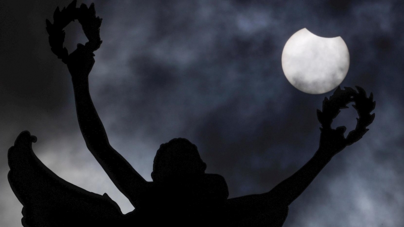 El eclipse solar parcial de este jueves se aprecia detrás de la estatua del parque del Jubileo en Bruselas, Bélgica.