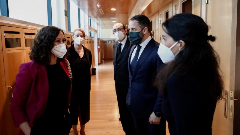 La presidenta de la Comunidad de Madrid, Isabel Díaz Ayuso (i) conversa con la portavoz de Vox en la Asamblea, Rocío Monasterio (d) en presencia del líder partido de ultradereha, Santiago Abascal (2d), en los pasillos de la Asamblea de Madrid, en una foto