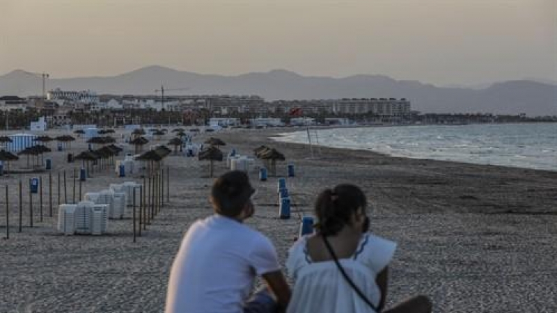 Dos jóvenes sentados contemplan la playa de la Malvarrosa durante la noche de San Juan en Valencia