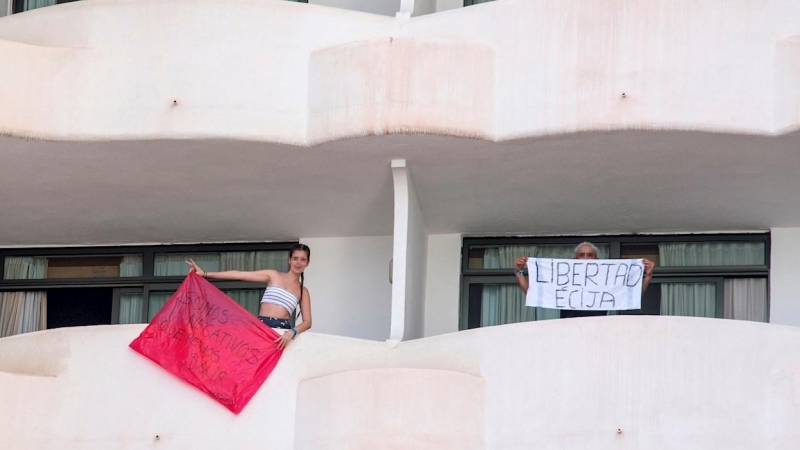 Dos jóvenes que permanecen en aislamiento en el hotel Palma Bellver de Palma portan dos pancartas pidiendo salir del hotel.