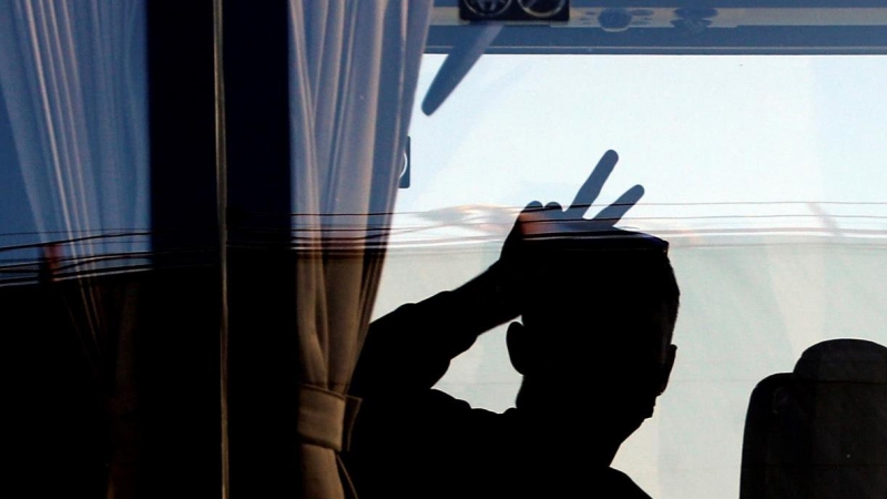 Una persona saluda desde el autobús tras desembarcar del ferry en el que viajaban 118 estudiantes que habían sido confinados en un hotel de Mallorca tras el macrobrote detectado en la isla.