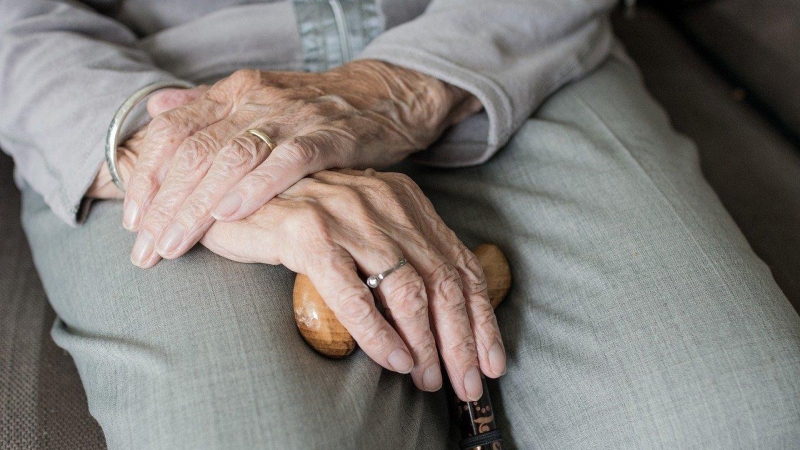 Una mujer mayor agarra entre sus manos un bastón.