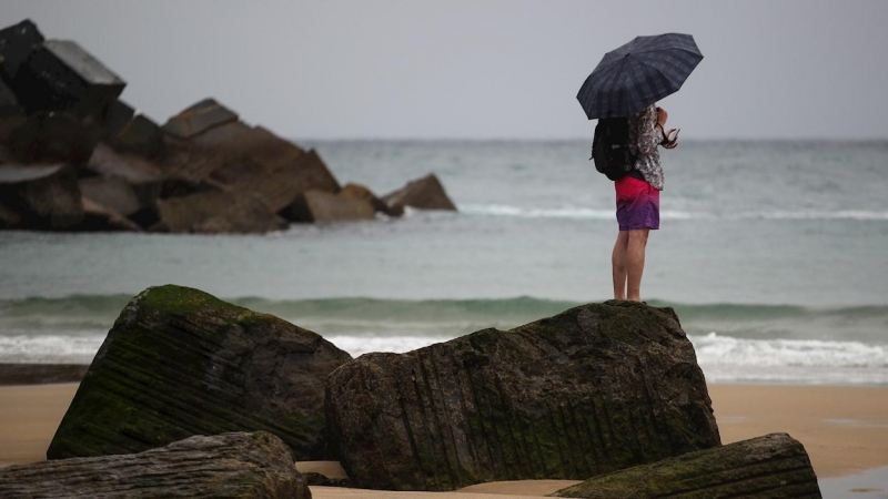 Un joven se protege con un paraguas en la playa de la Zurriola de San Sebastián.