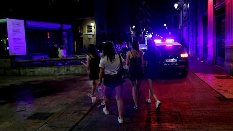 Varios jóvenes turistas pasan ante un coche de policía esta madrugada en la calle Caballeros del barrio de El Carmen de València.