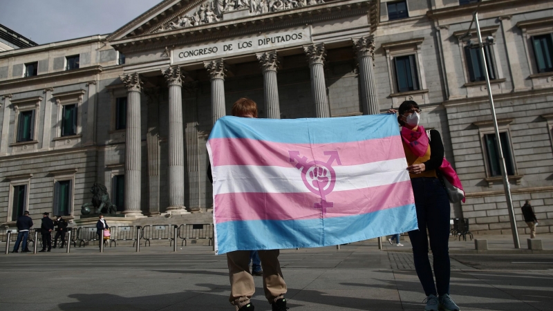 Dos personas so.stienen una bandera trans