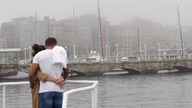 Una pareja observa el puerto de Gijón que amaneció este domingo con brumas.