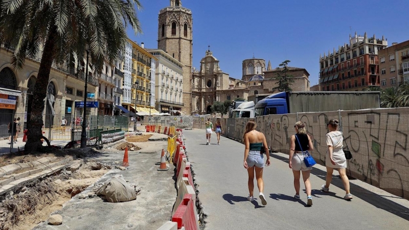 Varias turistas pasean por el asfaltado levantado y las vallas que rodean completamente la céntrica plaza de la Reina de València por las obras que se llevan a cabo para remodelarla.