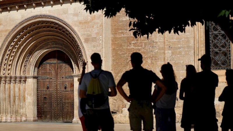 22/07/2021.- Un grupo de turistas atienden las explicaciones de su guía ante la puerta románica de la Catedral de Valencia.