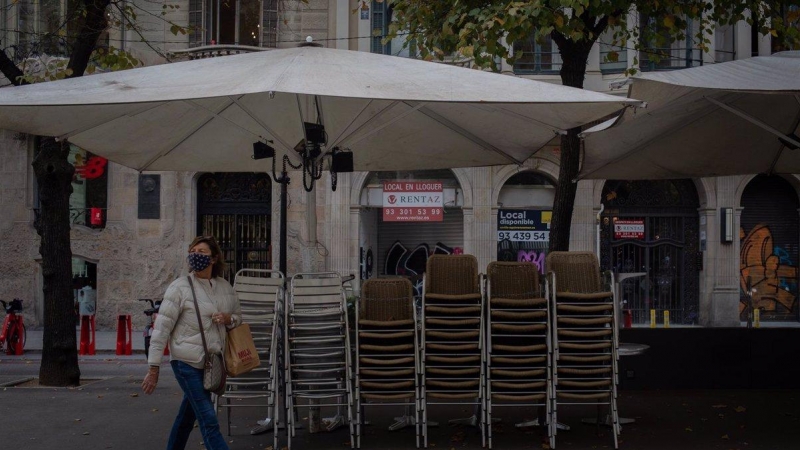 Una mujer pasa junto a la terraza recogida de un bar cerrado.