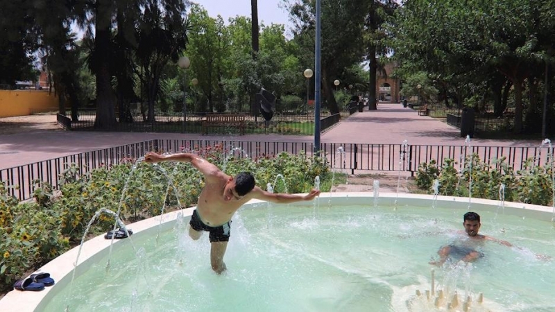 Dos jóvenes se refrescan en una fuente en el Jardín del Malecón de Murcia.