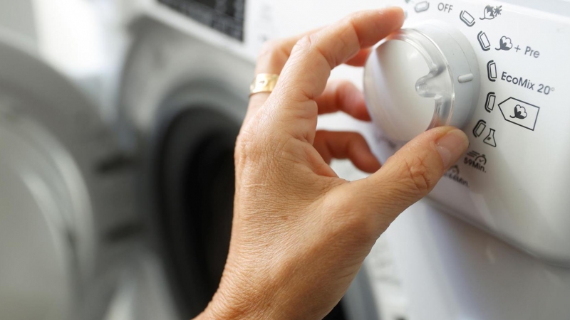 Una persona manipula una lavadora en plena escalada de los precios de la luz.