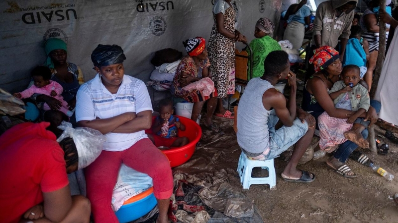 Las personas que perdieron sus hogares en el terremoto del pasado fin de semana en Haití se sientan bajo láminas de plástico en un campamento improvisado durante el paso de la tormenta tropical Grace.