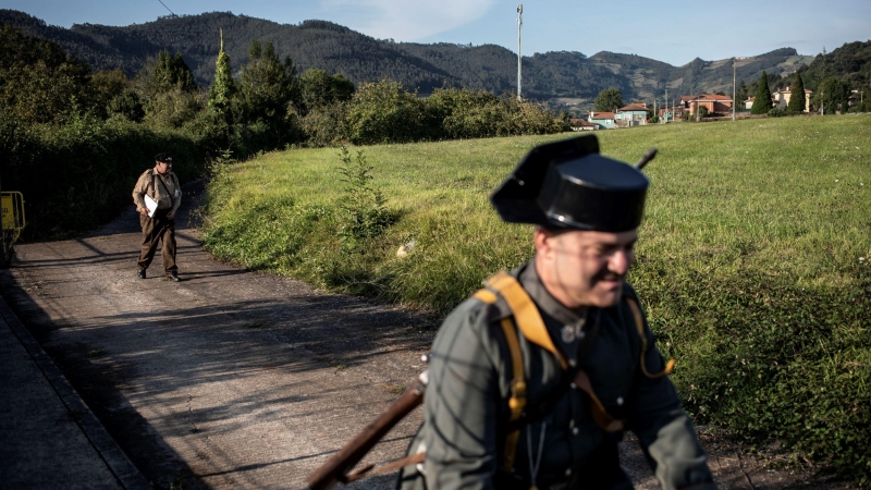 Voluntario vestido de Guardia Civil en bicicleta y Gudari vasco durante un descanso de la representación en   Grullos, Asturias, 11 de Septiembre, 2021.