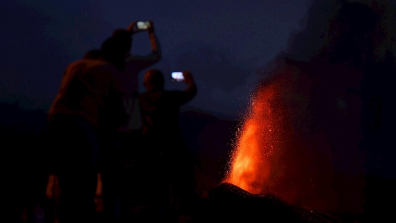 Cuatro personas contemplan desde una montaña al caer la noche la lava que sale del volcán de La Palma este lunes 20 de septiembre de 2021.