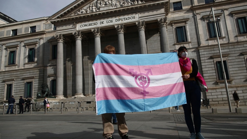 Dos personas sostienen una bandera trans durante una concentración convocada frente al Congreso de los Diputados en Madrid.