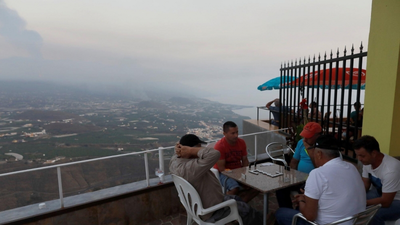 Los hombres juegan dominó en una terraza mirador, mientras el humo y la lava se muestran en el fondo, tras la erupción de un volcán en la isla canaria de La Palma, en Tijarafe.