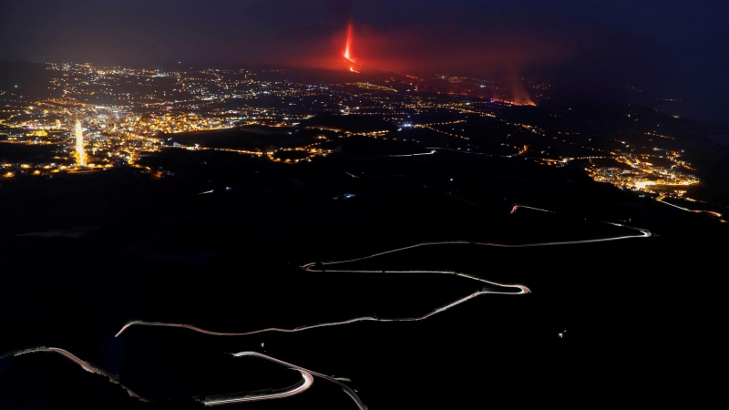 Vista del contraste de luces nocturnas de las poblaciones cercanas al volcán y el rojo de la lava en su discurrir hacia el mar desde Tijarafe (La Palma).