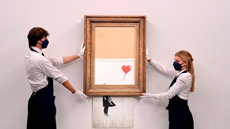 Empleados de la galería posan para los fotógrafos junto a la obra autodestruida de Banksy en la casa de subastas Sotheby's en Londres, Gran Bretaña, 03 de septiembre de 2021.