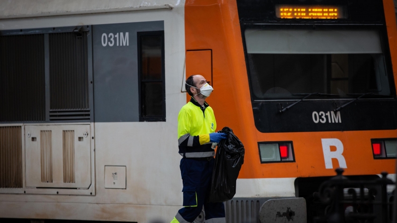 Un trabajador de la limpieza trabaja protegido con una mascarilla junto a un tren en Barcelona/Catalunya (España)