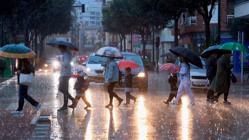 Varias personas cruzan una calle en Valencia bajo la lluvia.