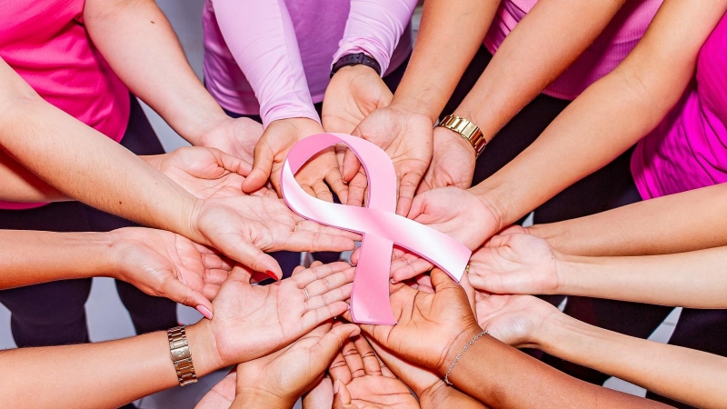 Mujeres sujetando un lazo rosa, símbolo de la lucha contra el cáncer de mama.