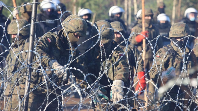 Una fotografía tomada el 9 de noviembre de 2021 muestra al personal de seguridad de Polonia detrás de una cerca de alambre de púas en la frontera entre Bielorrusia y Polonia.