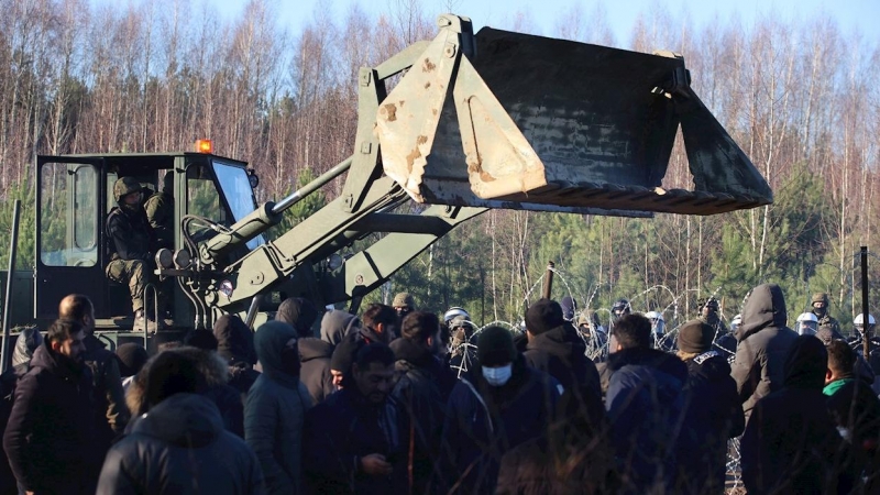 Un tractor maniobra en la frontera entre Bielorrusia y Polonia ante la mirada expectante de cientos de migrantes apostados frente a la alambrada que separa a ambos países.