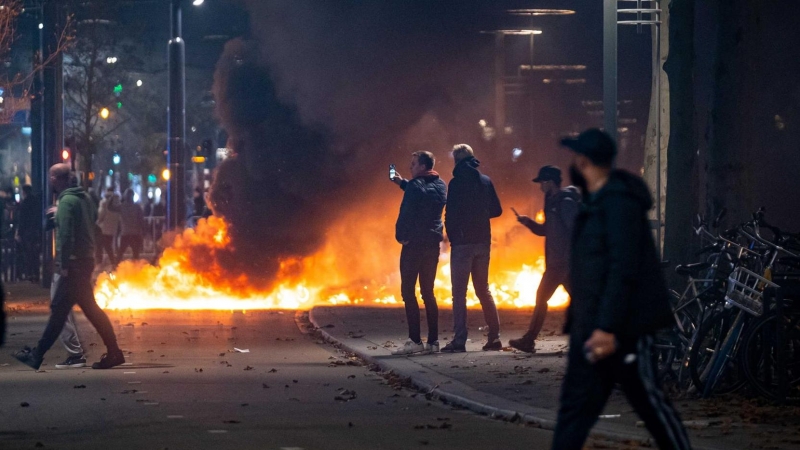 La gente se para cerca de objetos en llamas después de que una protesta  en Róterdam contra la 'política 2G' se convirtiera en disturbios