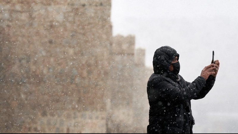 Un hombre se hace una foto con su teléfono móvil junto a la muralla de Ávila durante la primera nevada del otoño en la capital abulense.