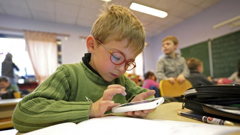 Un niño comprueba un dispositivo móvil durante una clase en un colegio.