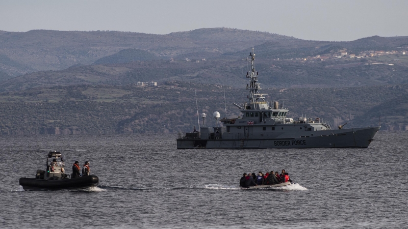Un bote salvavidas con refugiados llega a la isla griega de Lesbos, frente a la lancha patrullera de las tropas fronterizas británicas HMC Valiant, que forma parte de la misión Frontex.