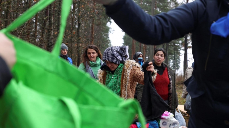 migrantes miran a través de la ropa entregada por la Cruz Roja Bielorrusa en el centro de transporte y logística cerca del puesto de control de Bruzgi en la frontera entre Bielorrusia y Polonia.