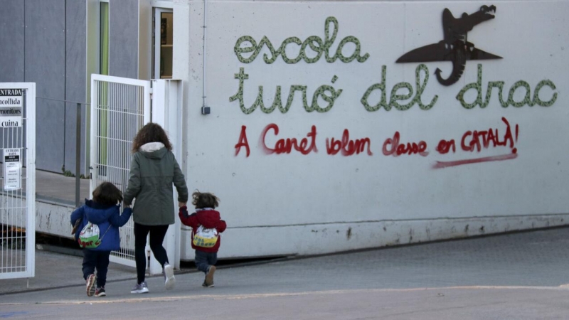 Una mare acompanya els seus fills a l'escola Turó del Drac de Canet de Mar. Una pintada reclama l'ensenyament en català a la façana del centre.