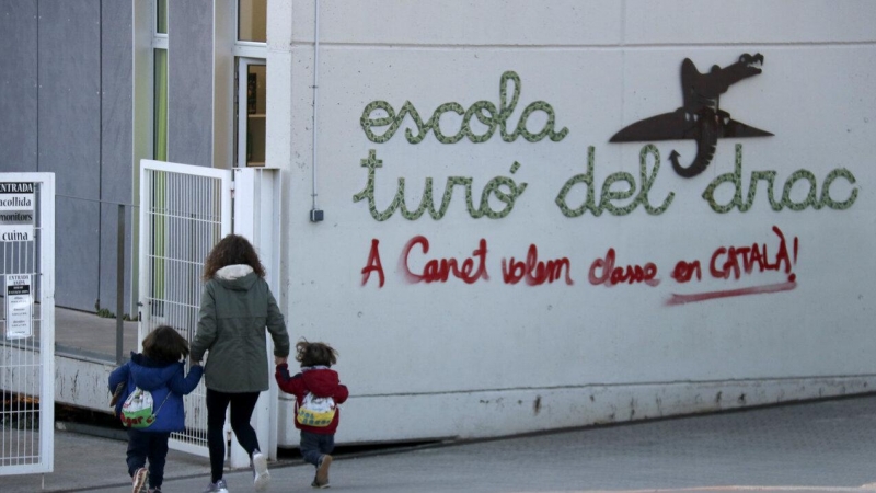 Una mare acompanya els seus fills a l'escola Turó del Drac de Canet de Mar. Una pintada reclama l'ensenyament en català a la façana del centre.
