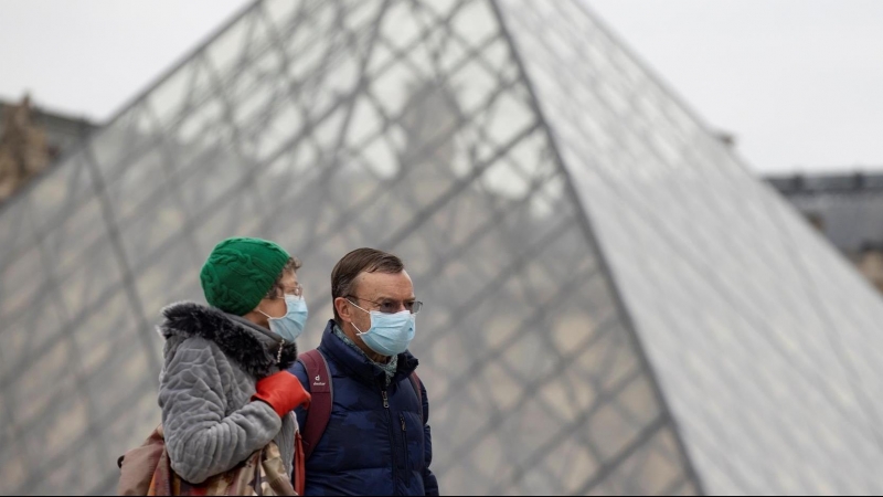 Peatones con mascarillas caminan junto a la pirámide del Louvre, este jueves en París.