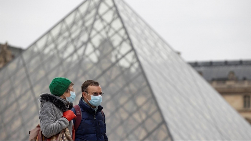 Peatones con mascarillas caminan junto a la pirámide del Louvre, este jueves en París.