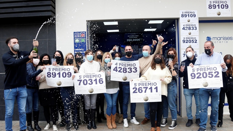 Trabajadores y vecinos de la administración número 3 de Manises, sita en la calle Maestro Guillem, muestran los números de los cinco premios que han vendido en su local.