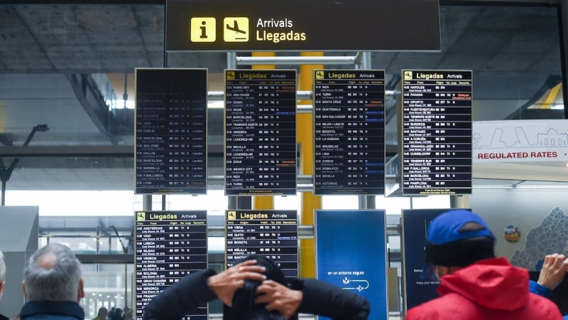 Varias personas observan los paneles de llegadas en el aeropuerto de Adolfo Suárez, un día previo a la Nochebuena, a 23 de diciembre de 2021, en Madrid.