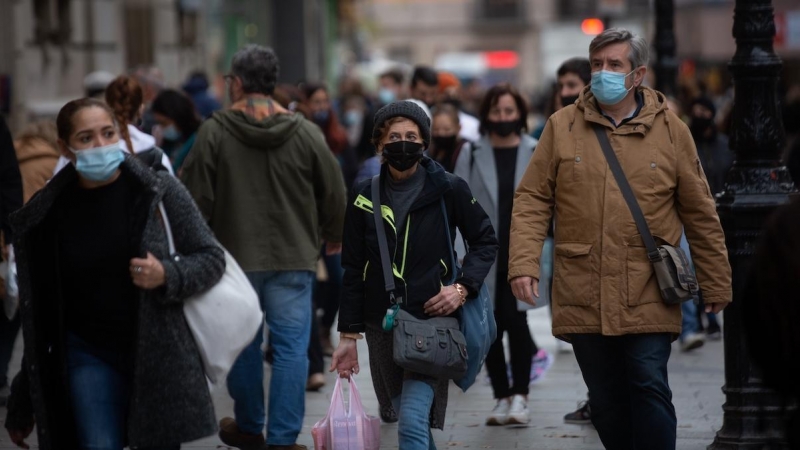 Viandantes caminan con bolsas por una vía de Barcelona, a 27 de diciembre de 2021.