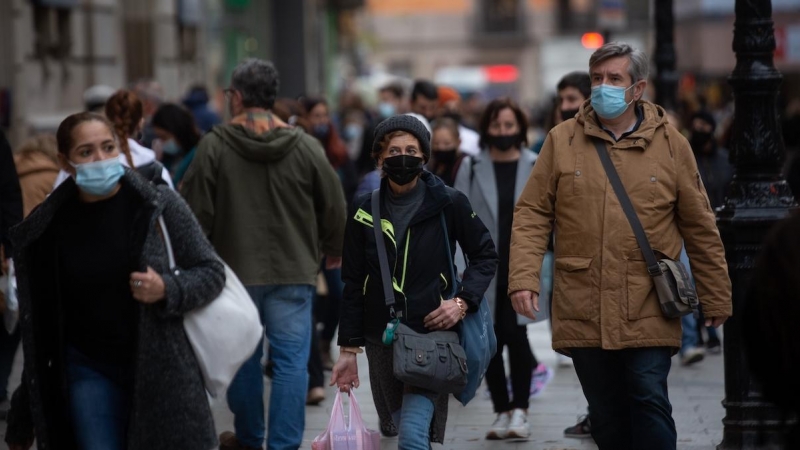 Viandantes caminan con bolsas por una vía de Barcelona, a 27 de diciembre de 2021.