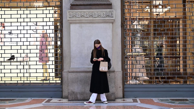 Una mujer con una máscara protectora mira su teléfono móvil mientras en un centro comercial cerca de la Piazza del Duomo, en Milán el 15 de marzo de 2021.