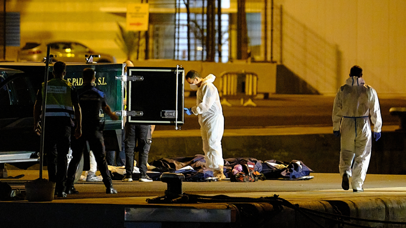 Dos agentes de Policía Portuaria, presencia como los trabajadores de la funeraria se llevan los cadáveres de las tres mujeres migrantes que naufragaron en alta mar en la costa de Lanzarote, en Puerto del Rosario de Fuerteventura, a 25 de agosto de 2021, e