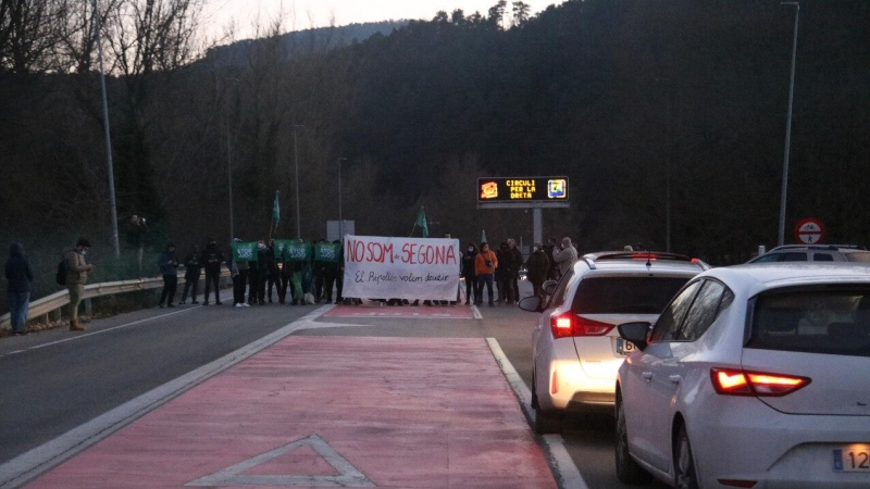 Els manifestants al fons protestant mentre els conductors esperen aturats pel tall de la carretera a Ripoll.